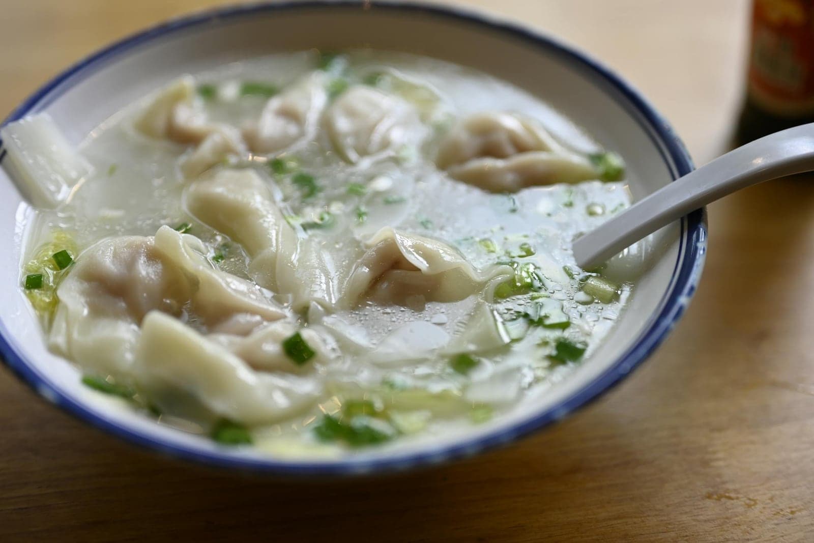 Wonton soup in a blue-rimmed bowl with dumplings, clear broth, and scallions