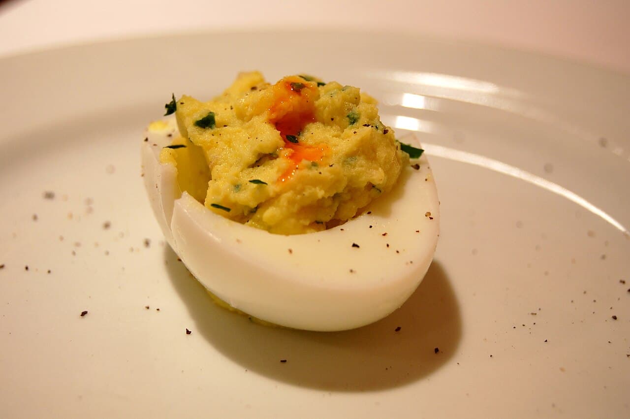 Deviled eggs on a platter topped with golden crispy fried capers and smoked paprika