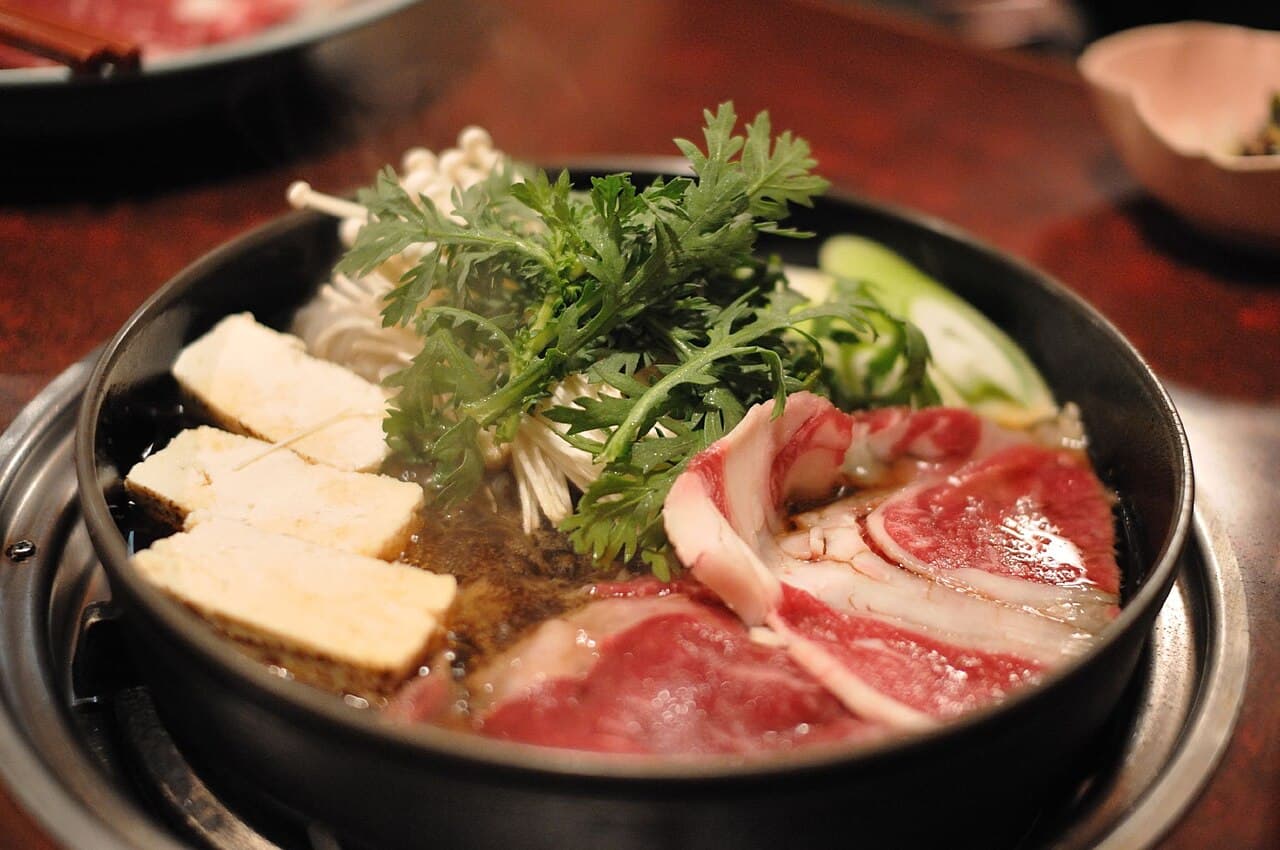 Sukiyaki hot pot with thinly sliced beef, tofu, mushrooms, and vegetables in sweet-savory broth