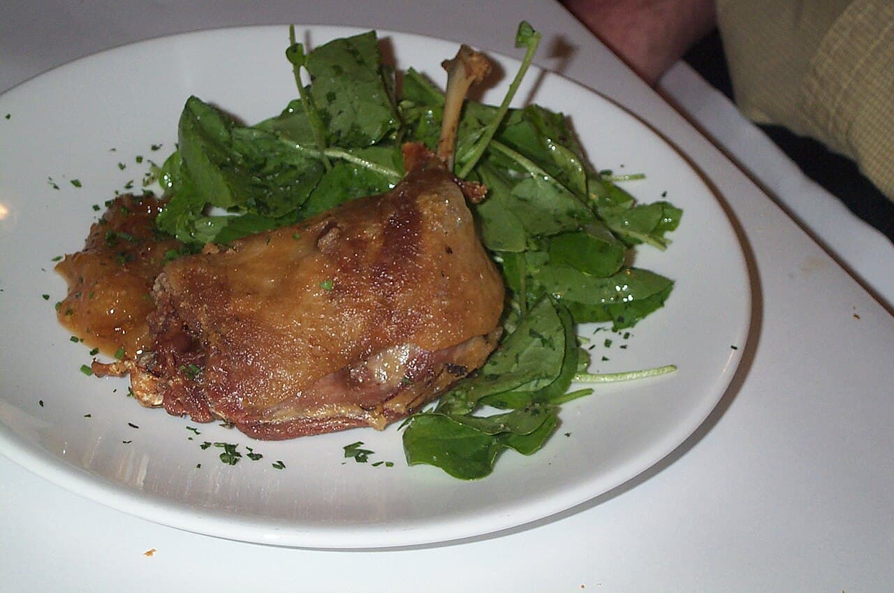 Crisp-skinned duck confit leg with golden potatoes on a white plate