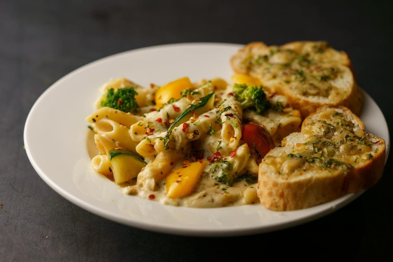 Garlic butter pasta with penne, vegetables, and toasted garlic bread on a white plate