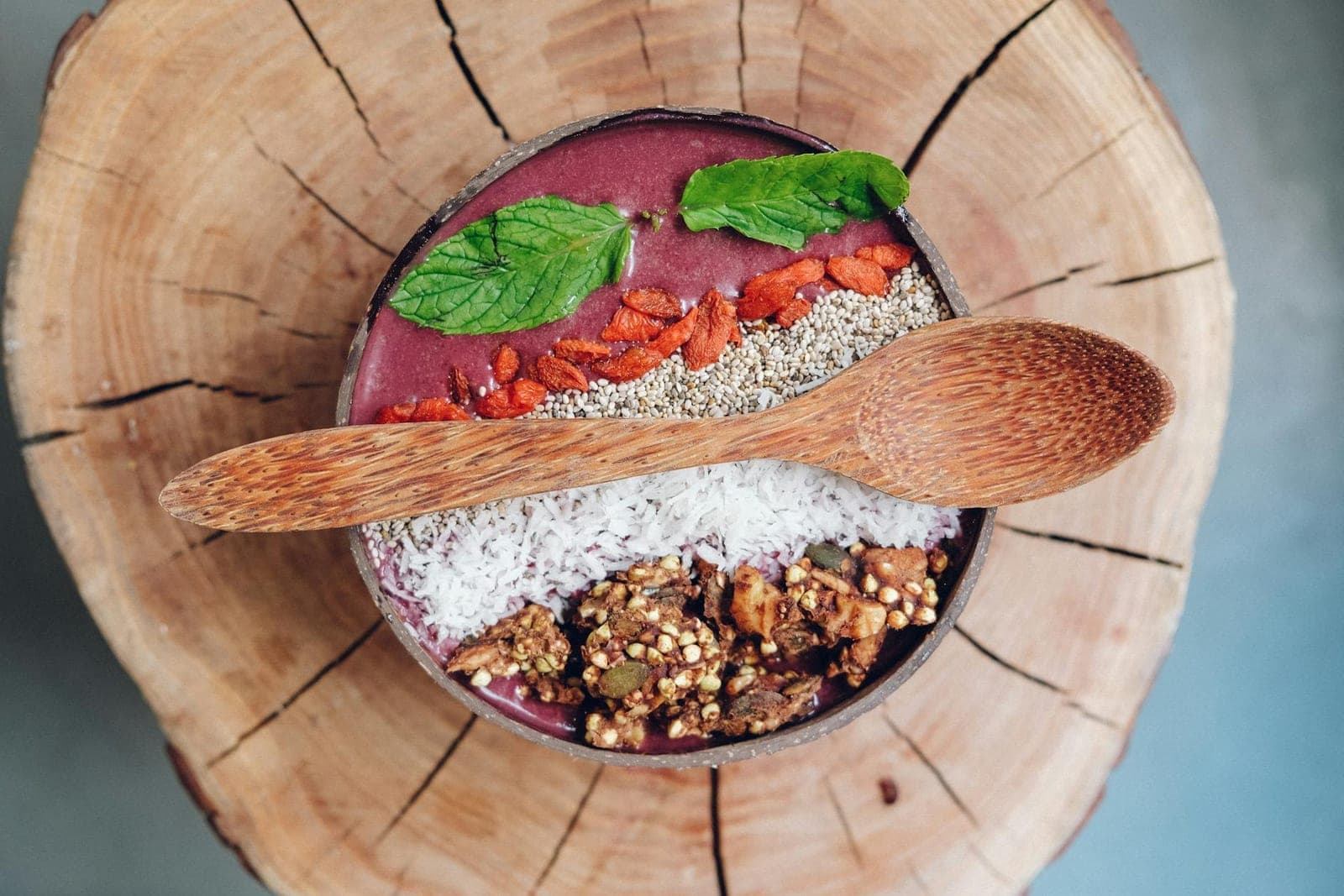 Acai protein bowl topped with granola, berries, chia seeds, and mint in a wooden bowl