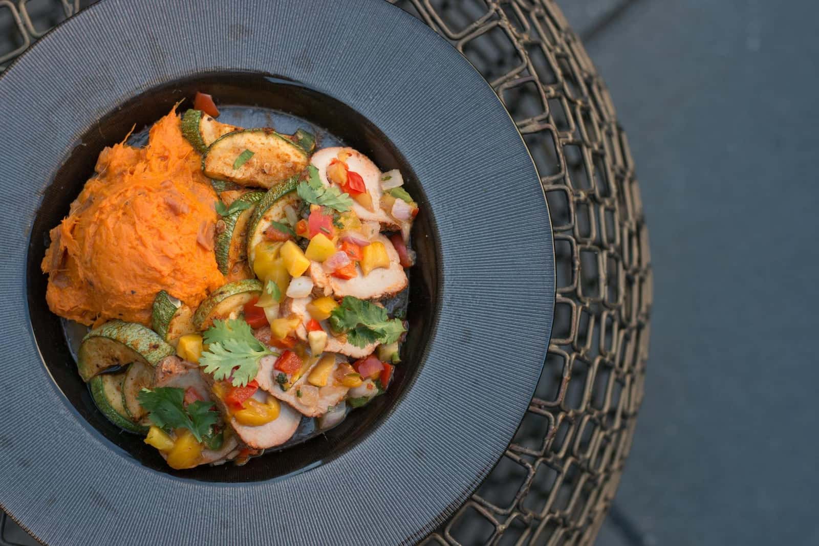 BBQ chicken sweet potato bowl with chicken, vegetables, and orange sweet potato mash on a dark plate