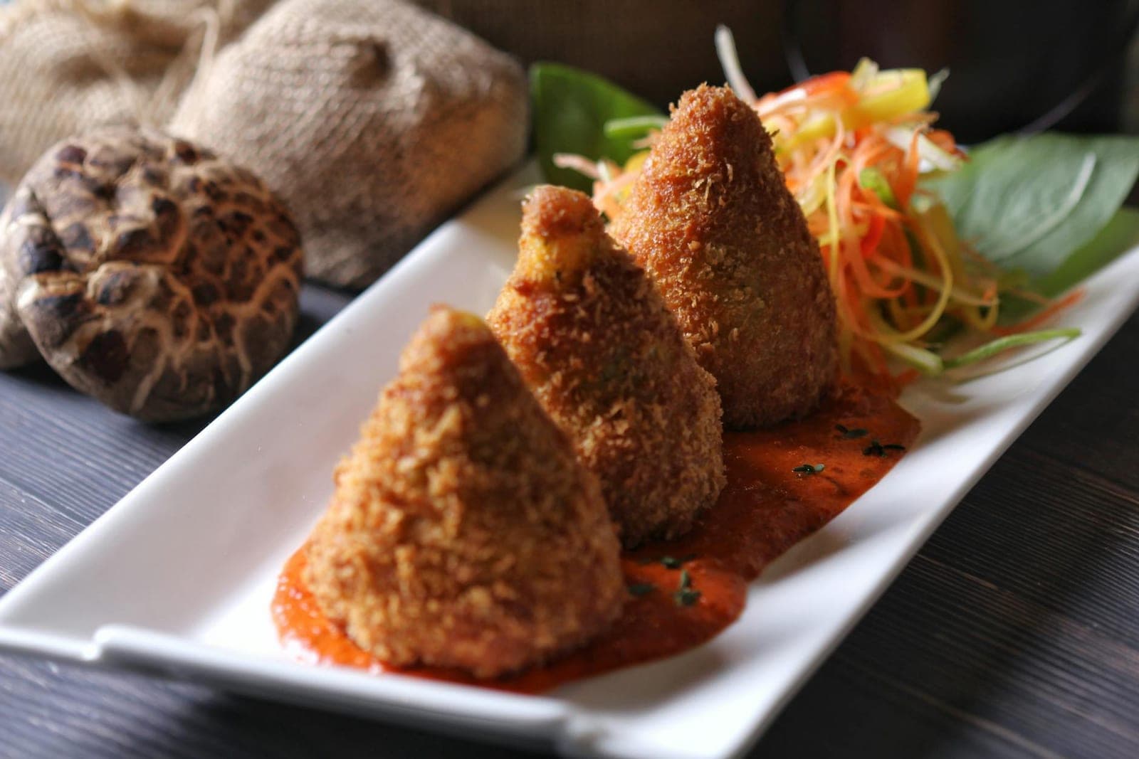 Arancini Sicilian rice balls with crisp coating, sauce, and salad on a white plate