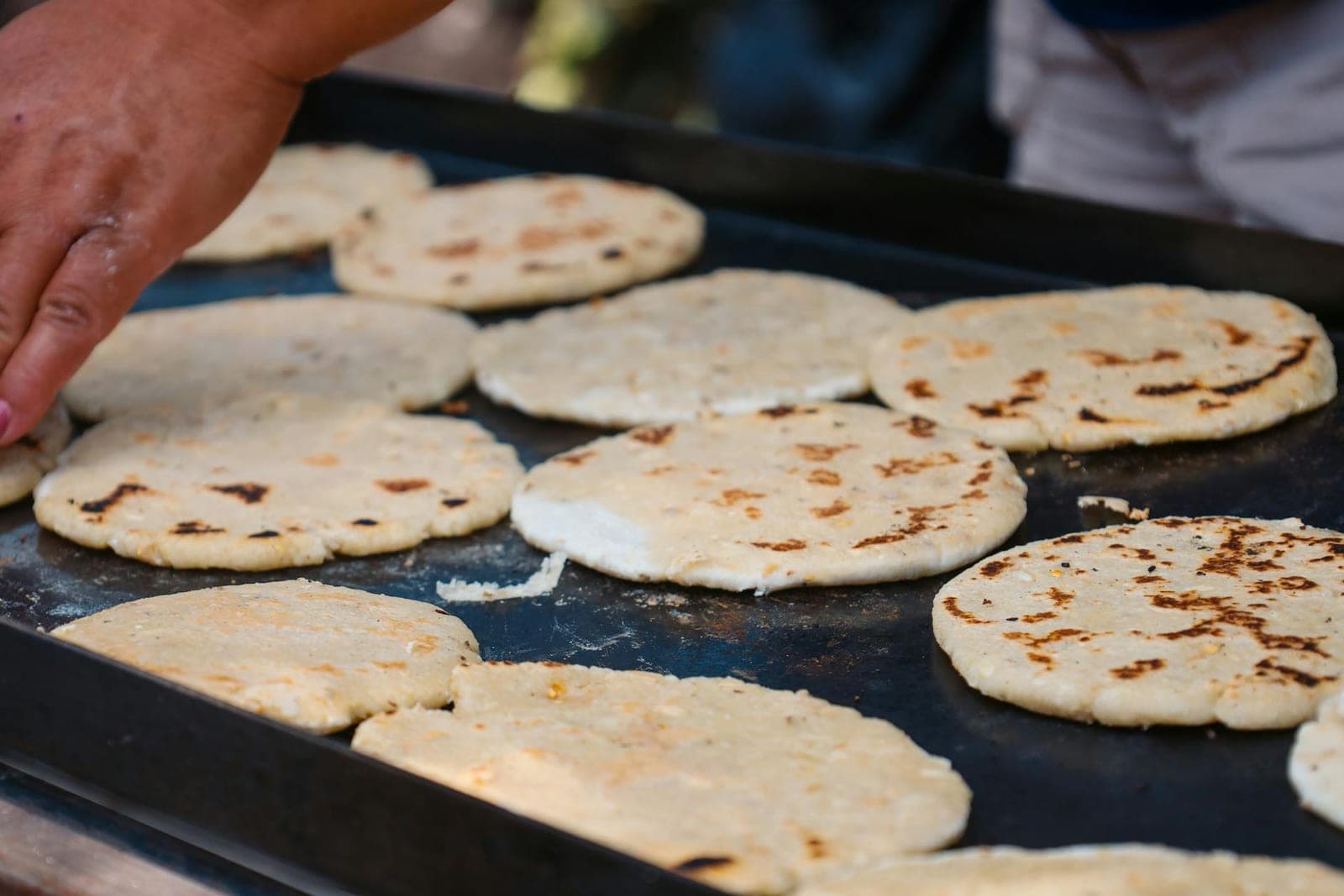 Arepas corn cakes cooking on a hot griddle with browned spots