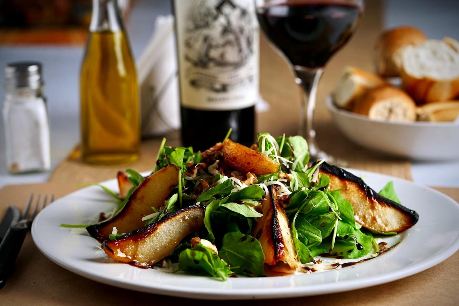 Arugula pear salad with sliced pears, greens, bread, and dressing on a white plate