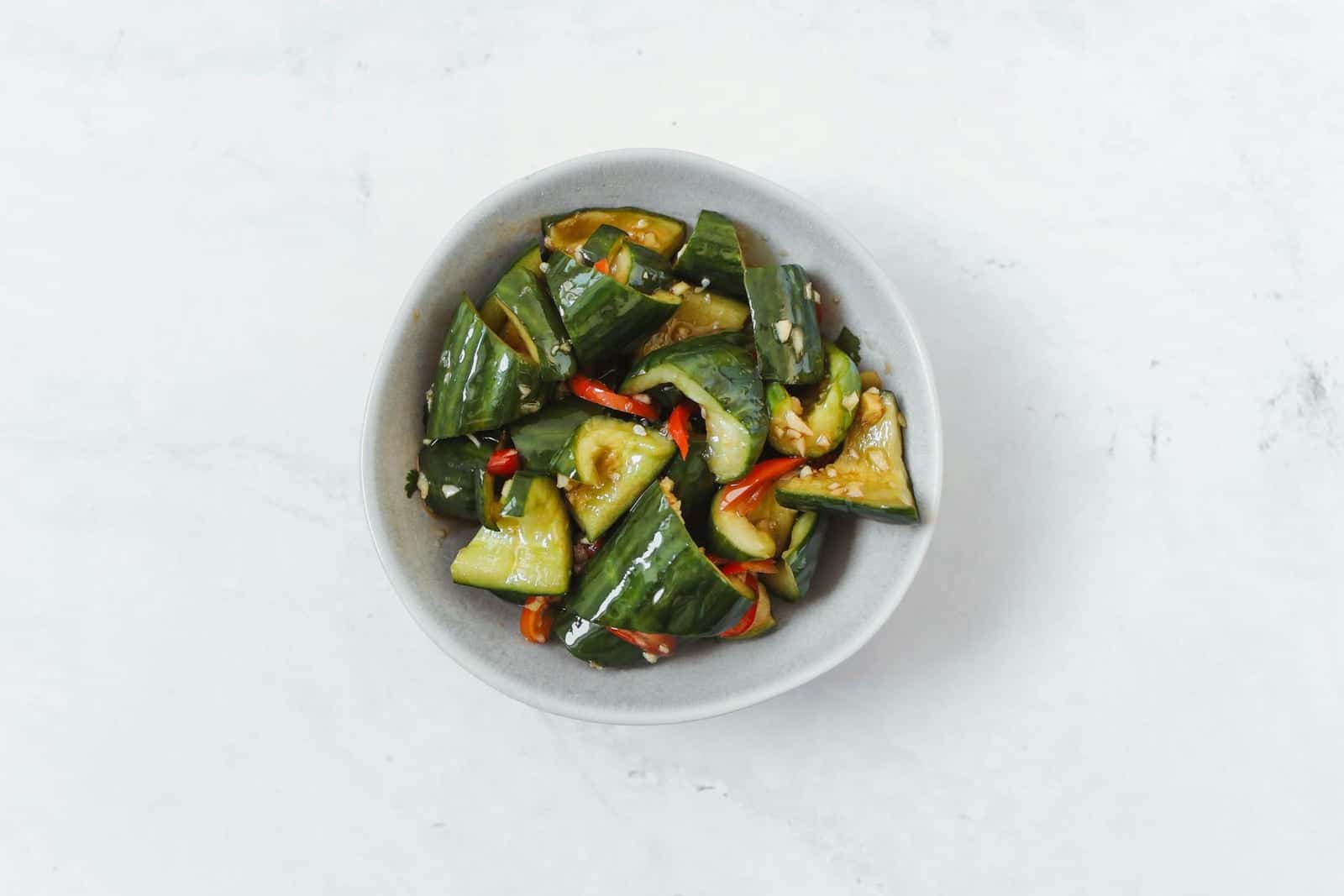 Asian cucumber salad with sliced cucumbers, red chiles, and dressing in a small bowl