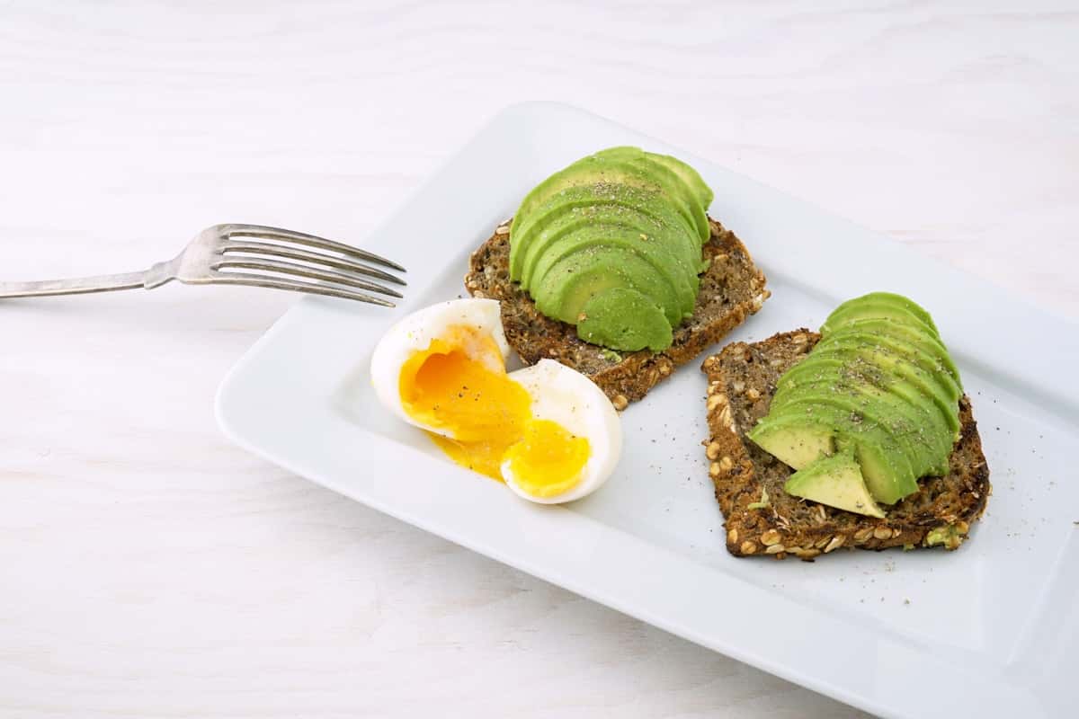 Avocado toast variations with sliced avocado and soft-boiled egg on seeded bread
