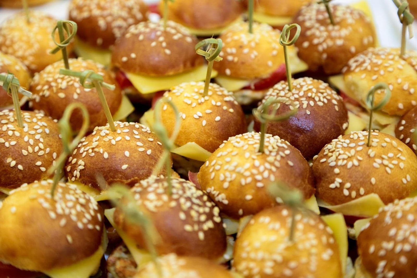 Bacon cheeseburger sliders with sesame buns, cheese, and skewers on a tray