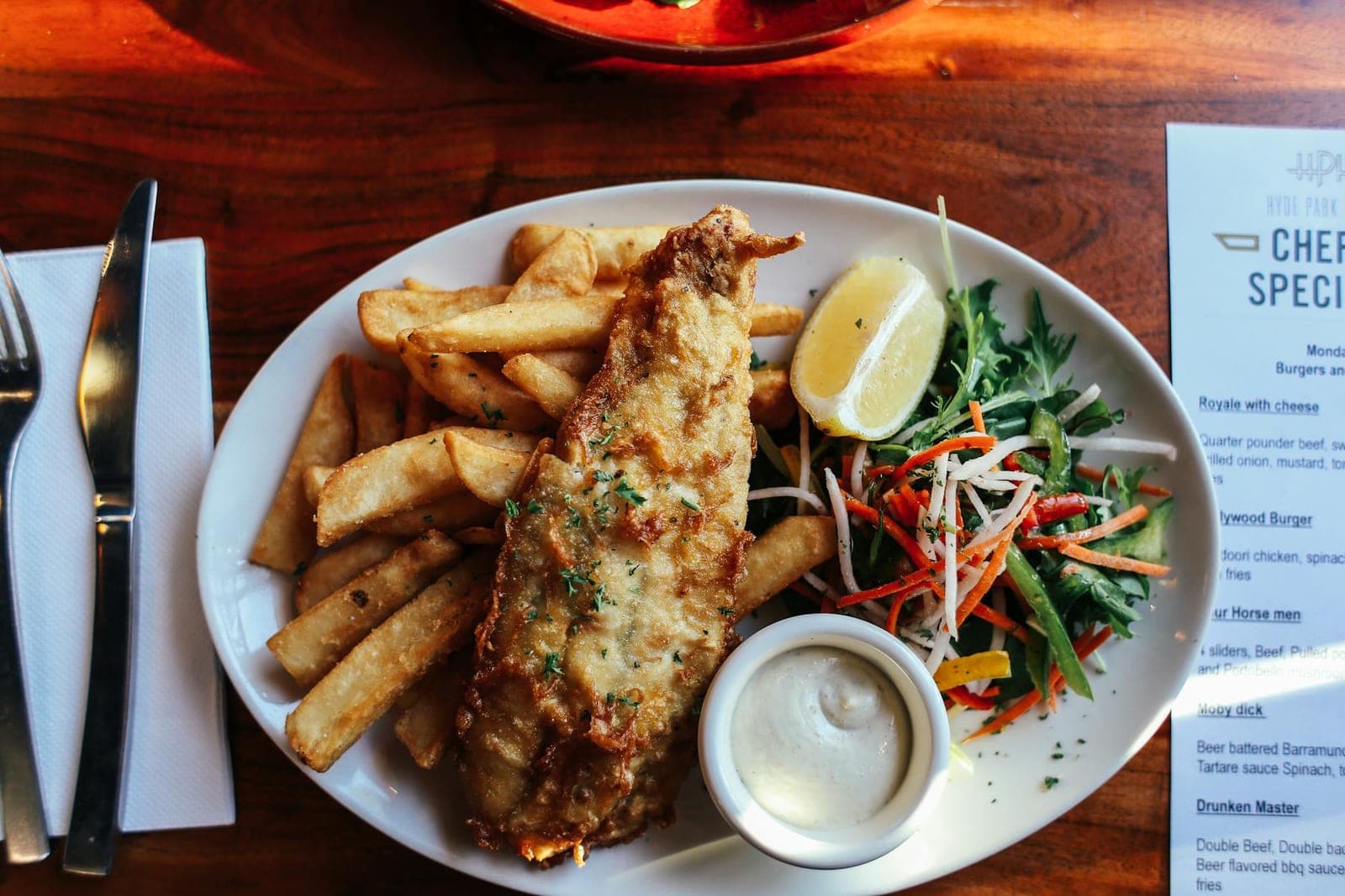 Baked fish and chips with tartar sauce, lemon, fries, and salad on a restaurant plate