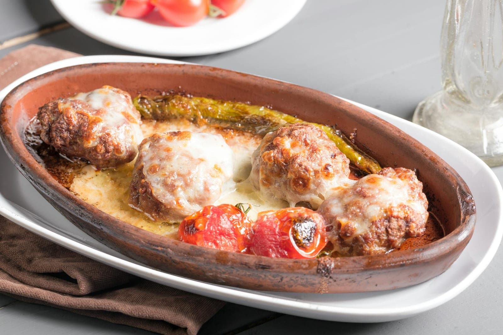 Baked turkey meatballs in tomato sauce with peppers and melted cheese in a clay baking dish