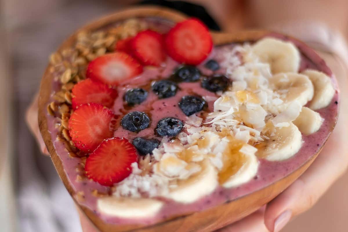 Smoothie bowl with a creamy banana base topped with sliced bananas, berries, granola, chia seeds, and a drizzle of peanut butter