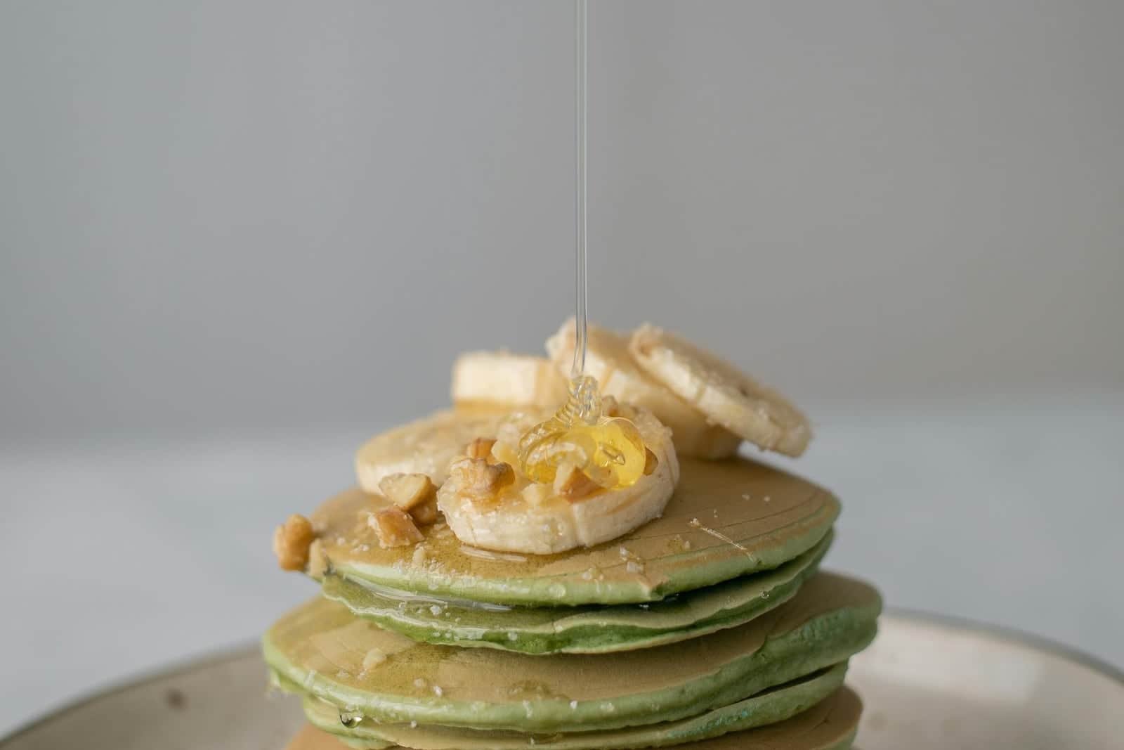Banana protein pancakes stacked with banana slices and honey on a plate