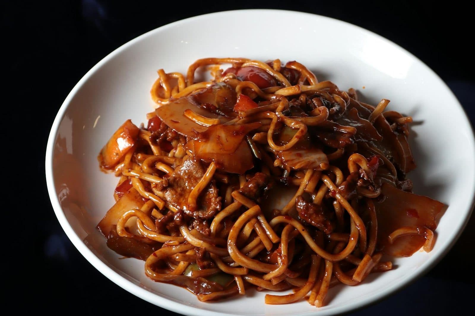 Beef chow fun noodles stir-fried with beef, vegetables, and savory sauce on a white plate