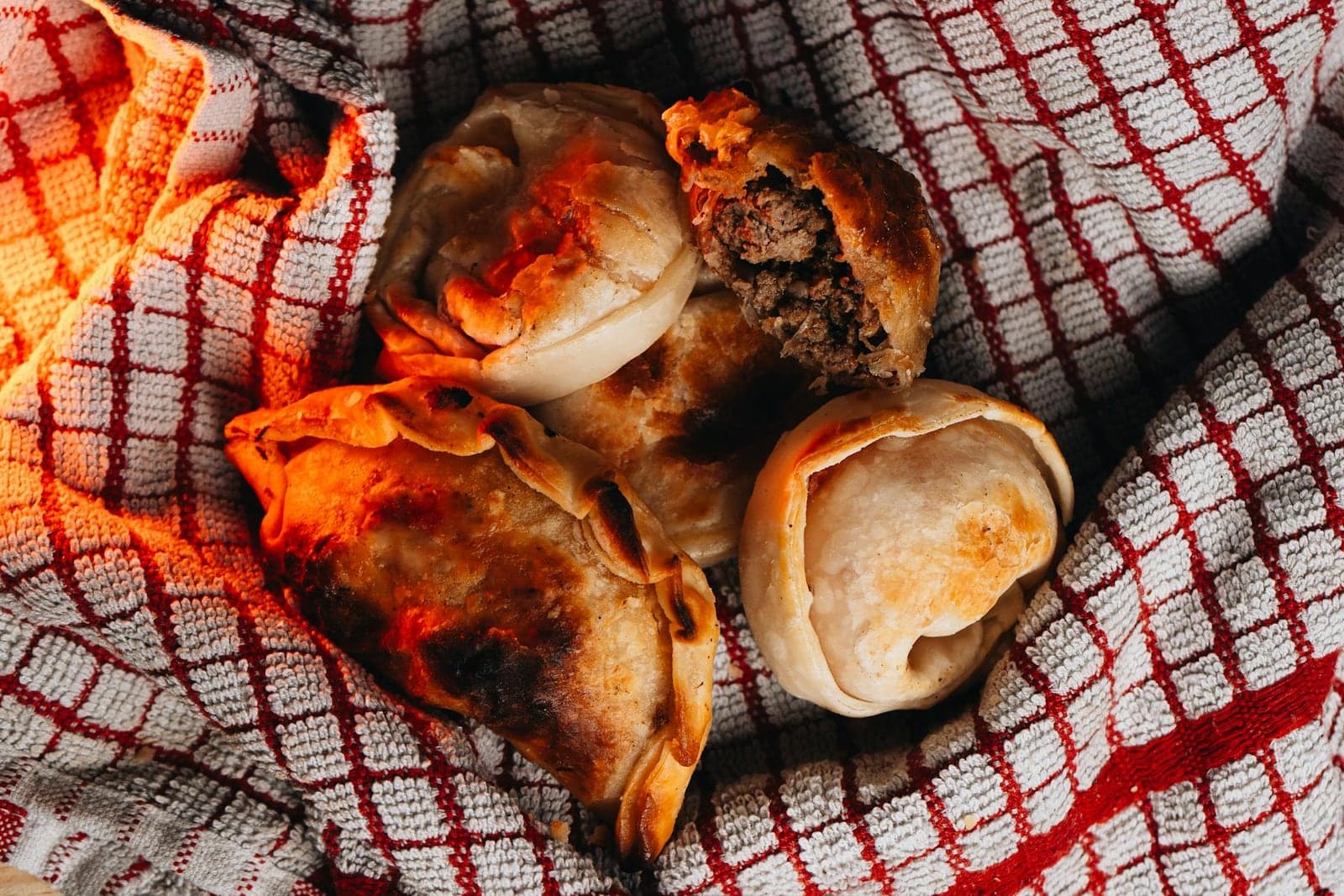 Beef empanadas with browned pastry and savory filling on a red checkered cloth