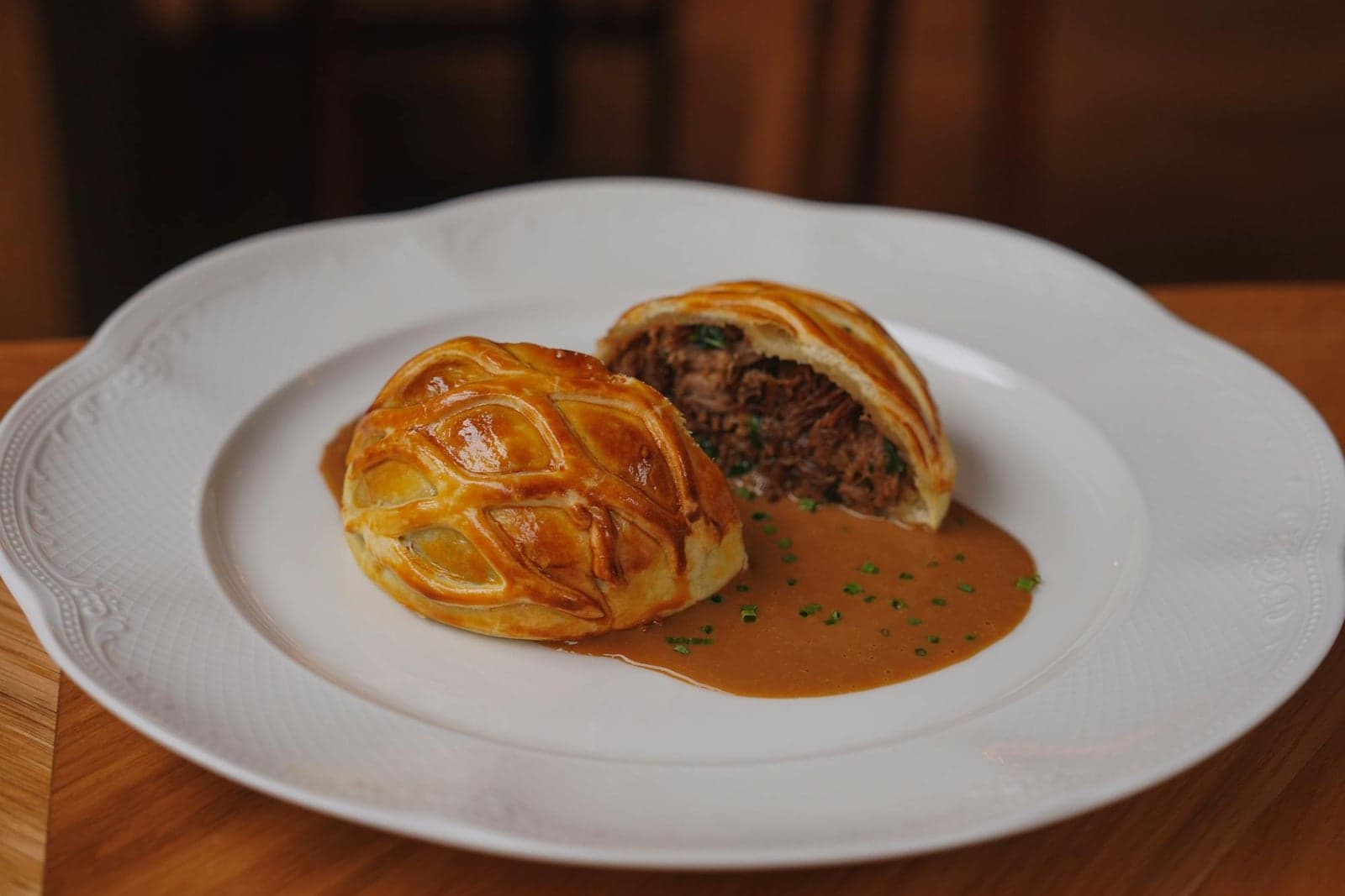 Beef Wellington slices in golden puff pastry served with sauce on a white plate