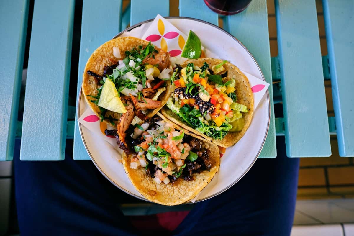Three black bean tacos on a plate topped with cabbage slaw, avocado, and drizzled with chipotle crema