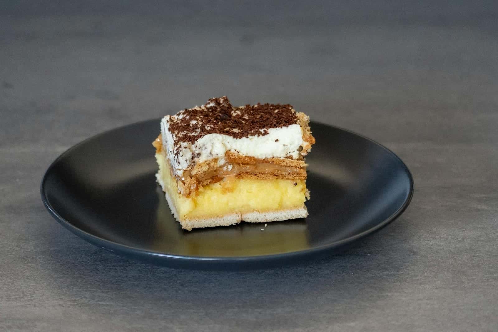 Boston cream pie-style cake slice with custard layer and chocolate topping on a black plate
