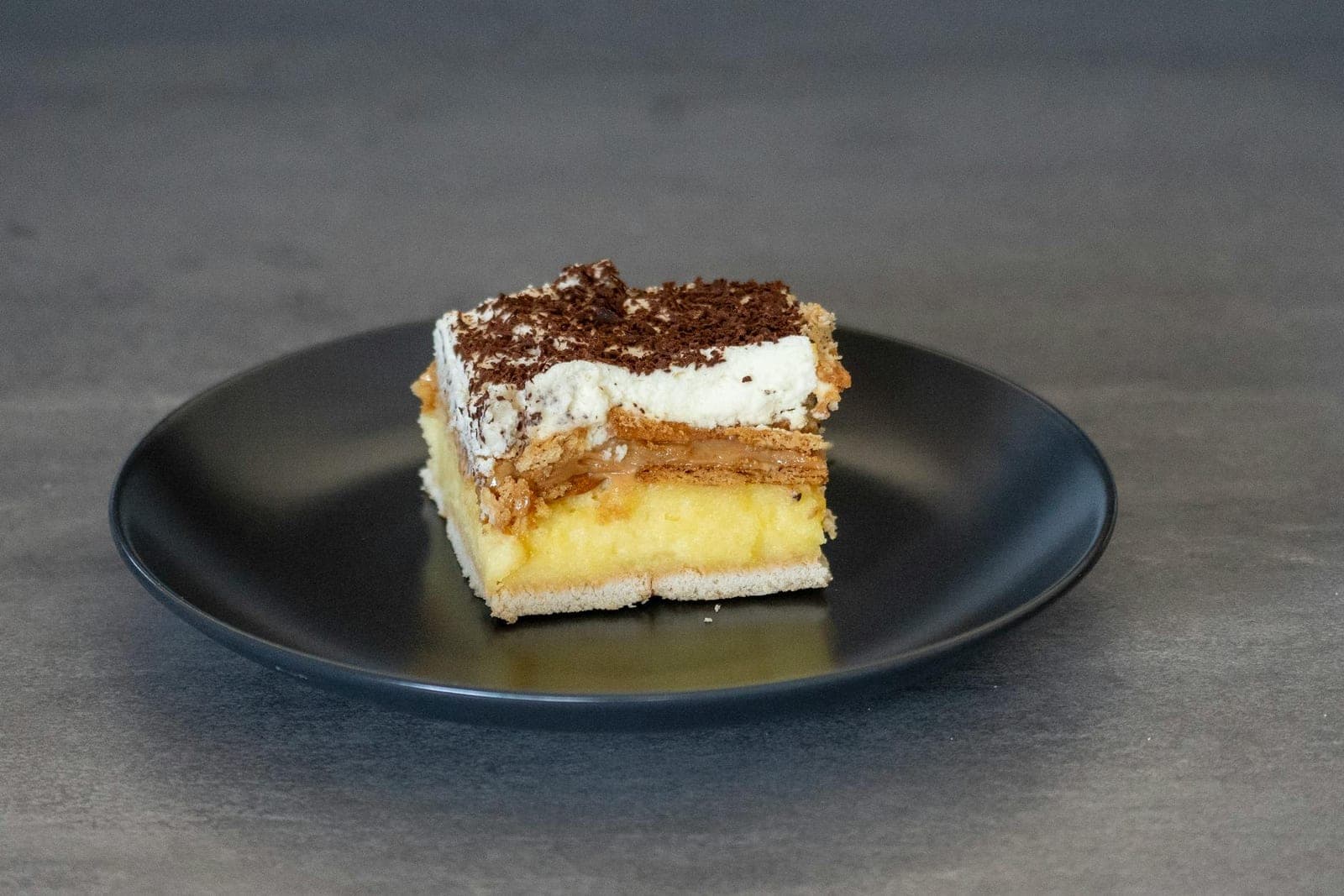 Boston cream pie-style cake slice with custard layer and chocolate topping on a black plate