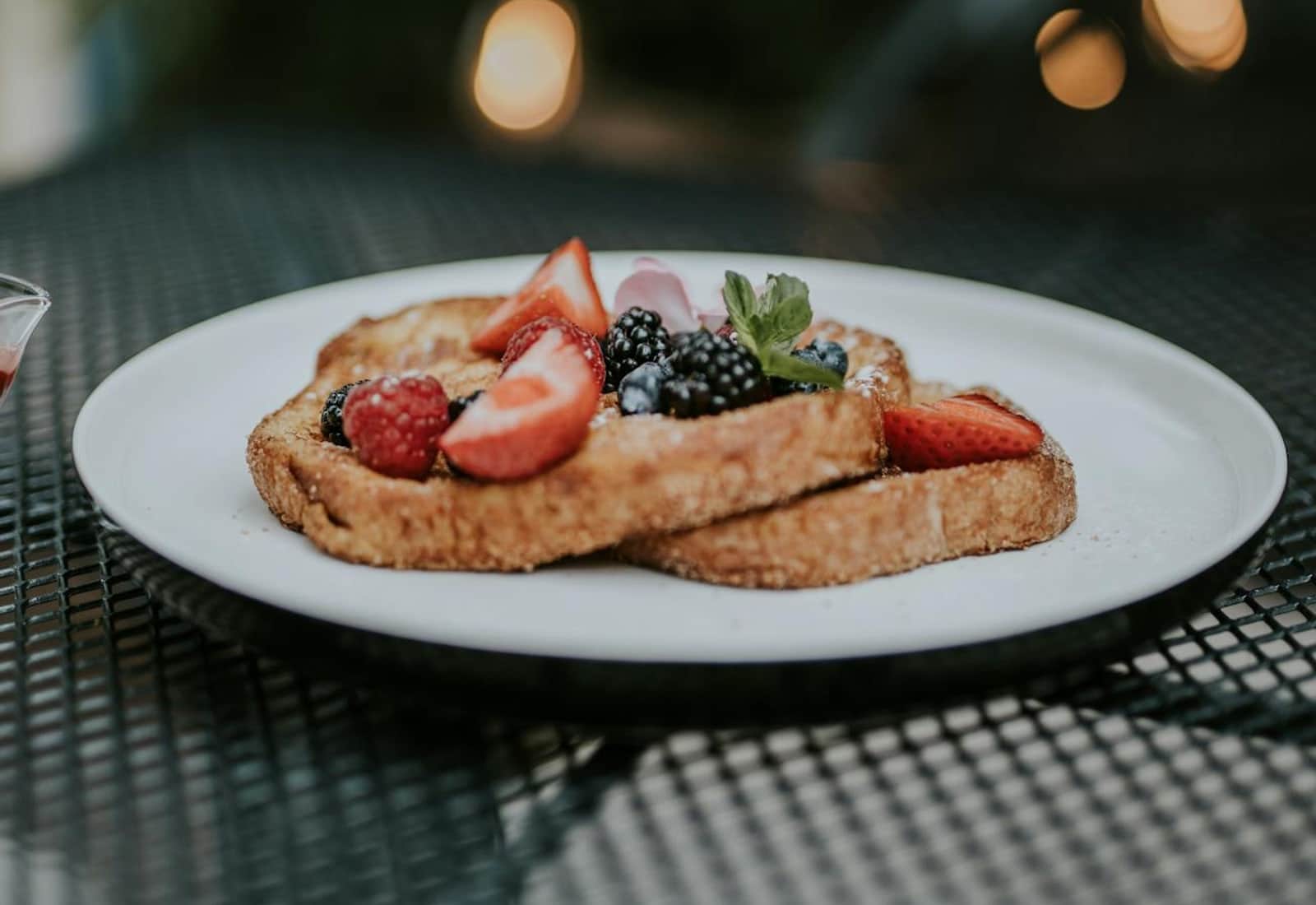 Brioche French toast with berries, cream, and fresh fruit on a white plate