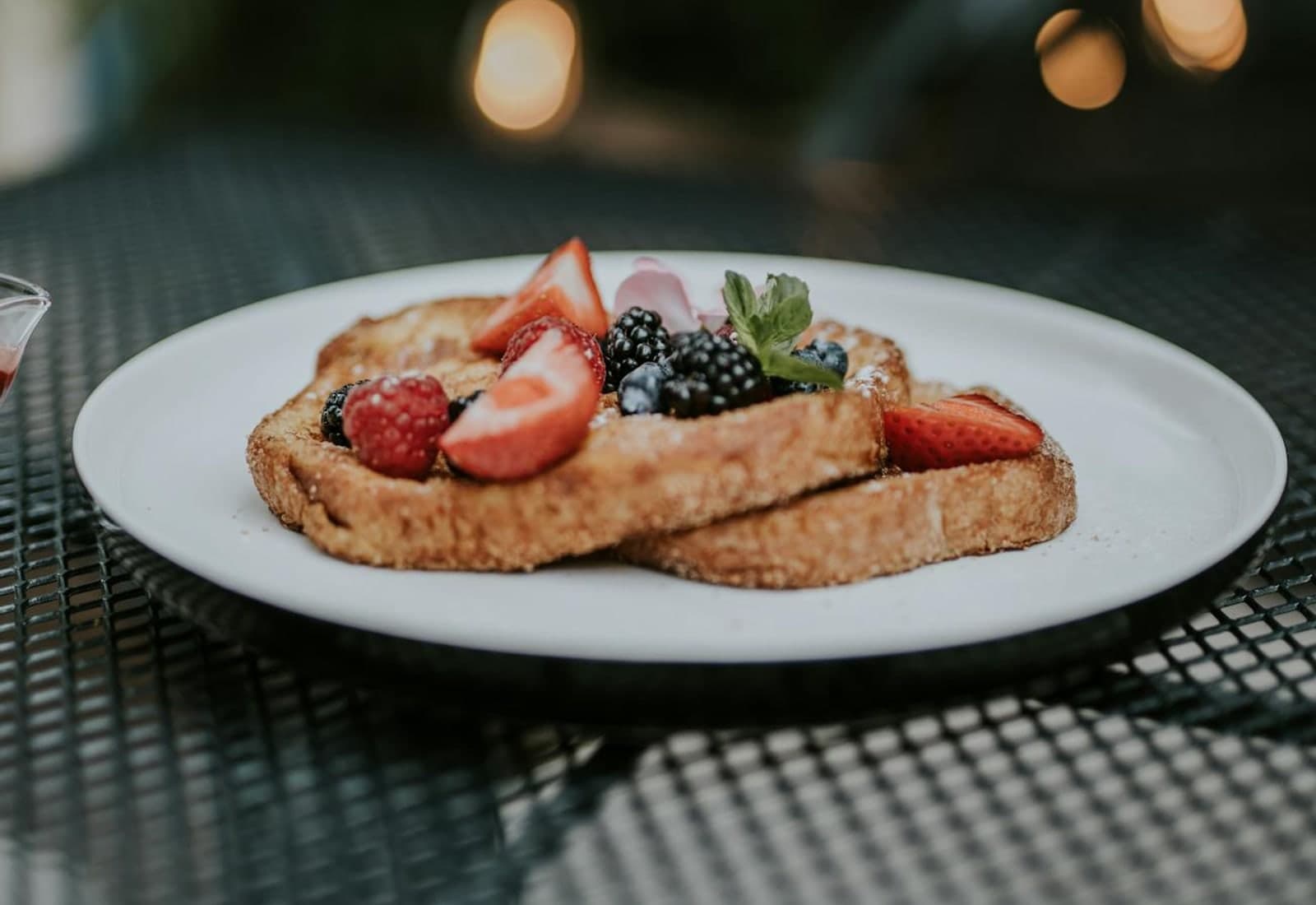 Brioche French toast with berries, cream, and fresh fruit on a white plate
