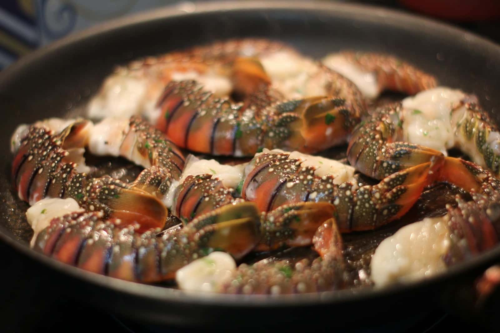 Broiled lobster tails with garlic butter and herbs sizzling in a pan