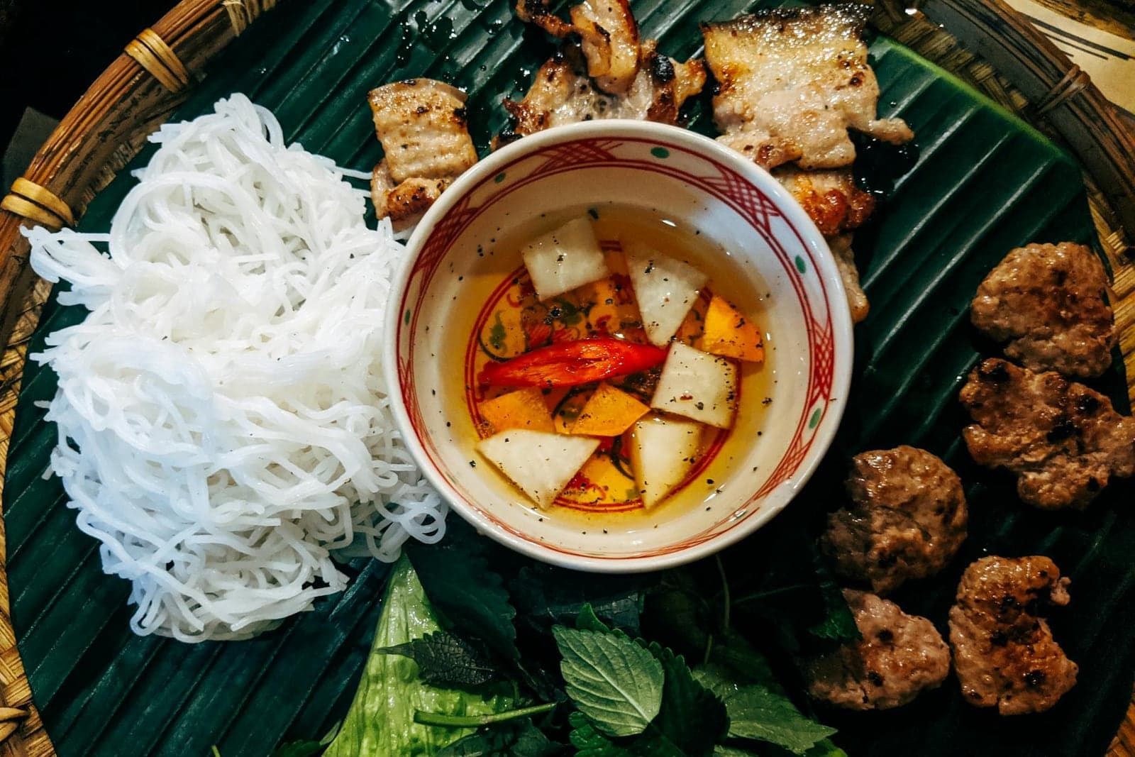 Bun cha Hanoi with grilled pork, rice noodles, herbs, and dipping sauce on banana leaf