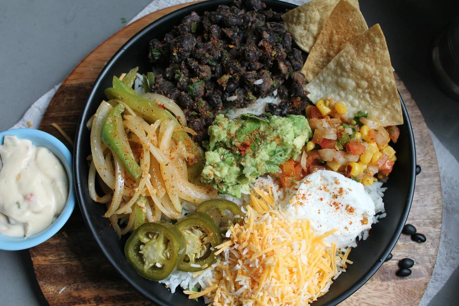 Burrito bowl meal prep with black beans, rice, guacamole, cheese, jalapenos, and salsa
