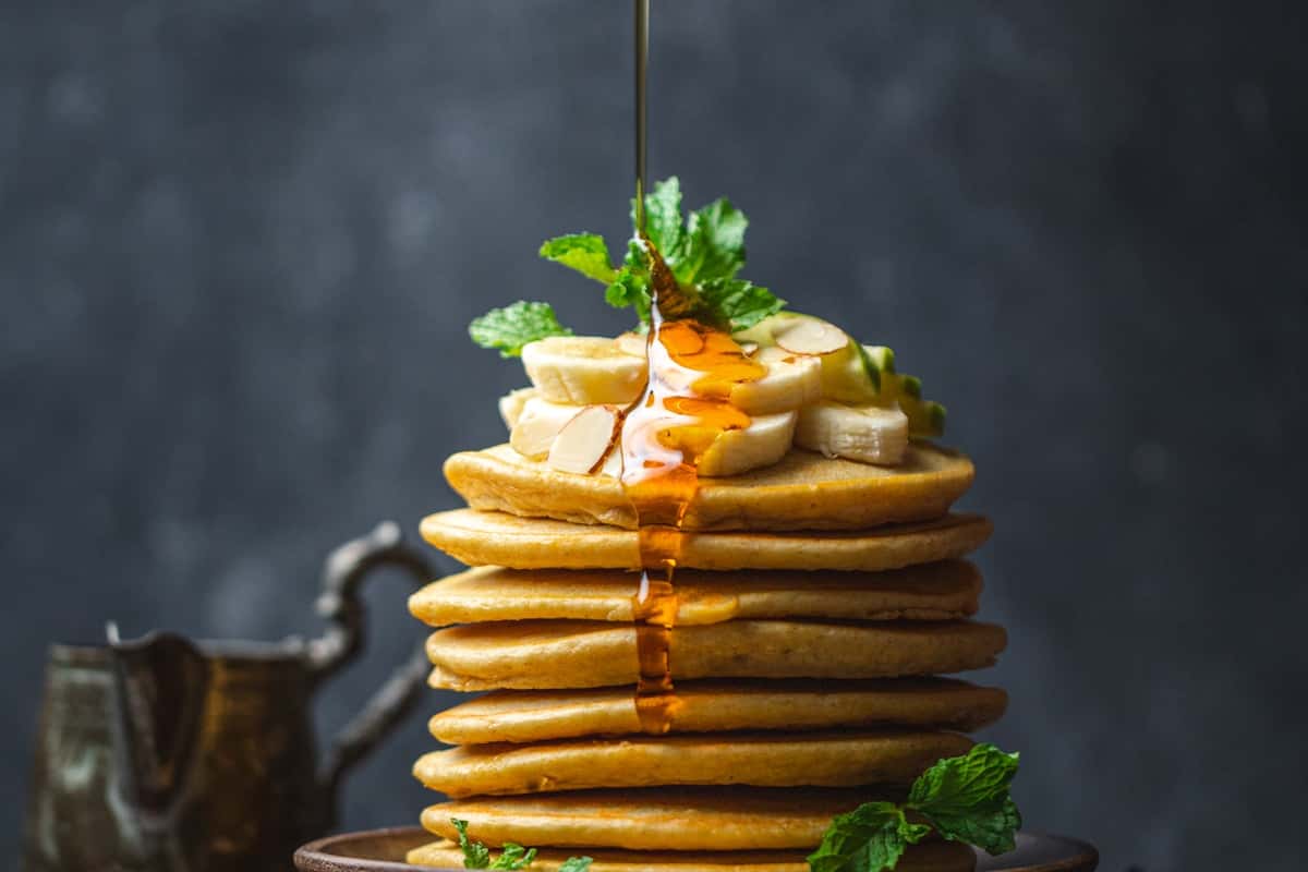 Stack of fluffy pancakes with banana slices and maple syrup