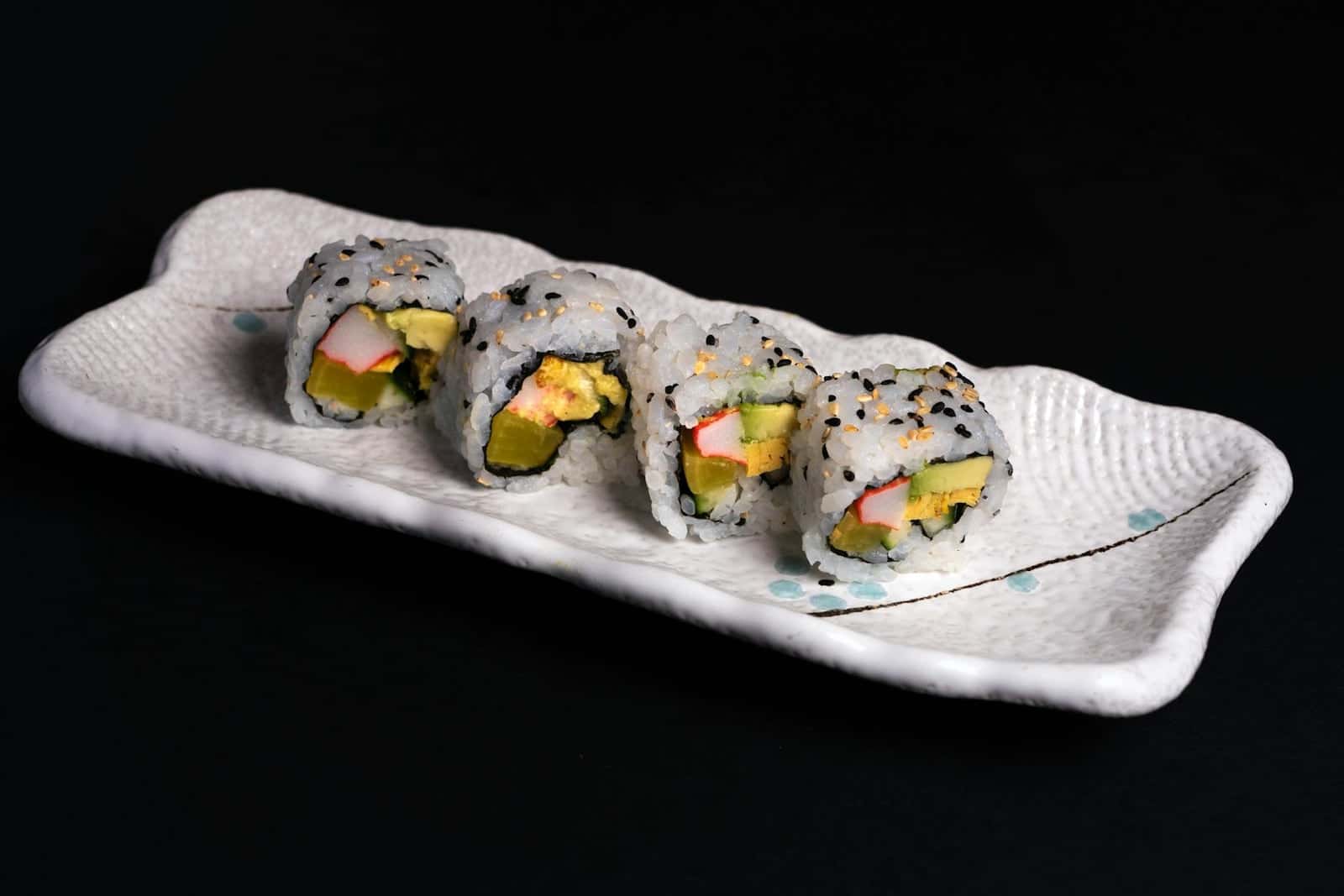 California sushi rolls with avocado, crab-style filling, sesame, and chopsticks on a white plate