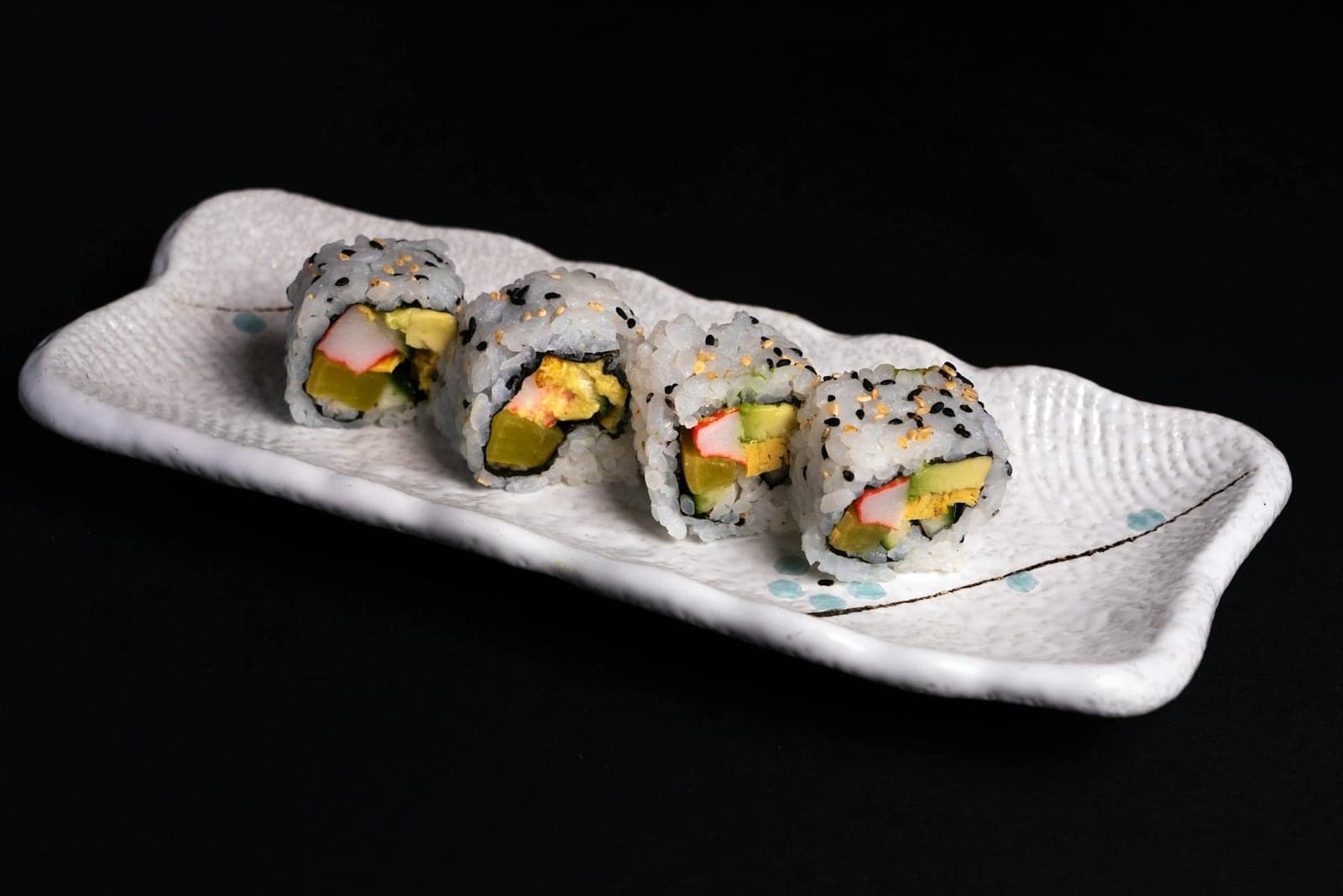 California sushi rolls with avocado, crab-style filling, sesame, and chopsticks on a white plate