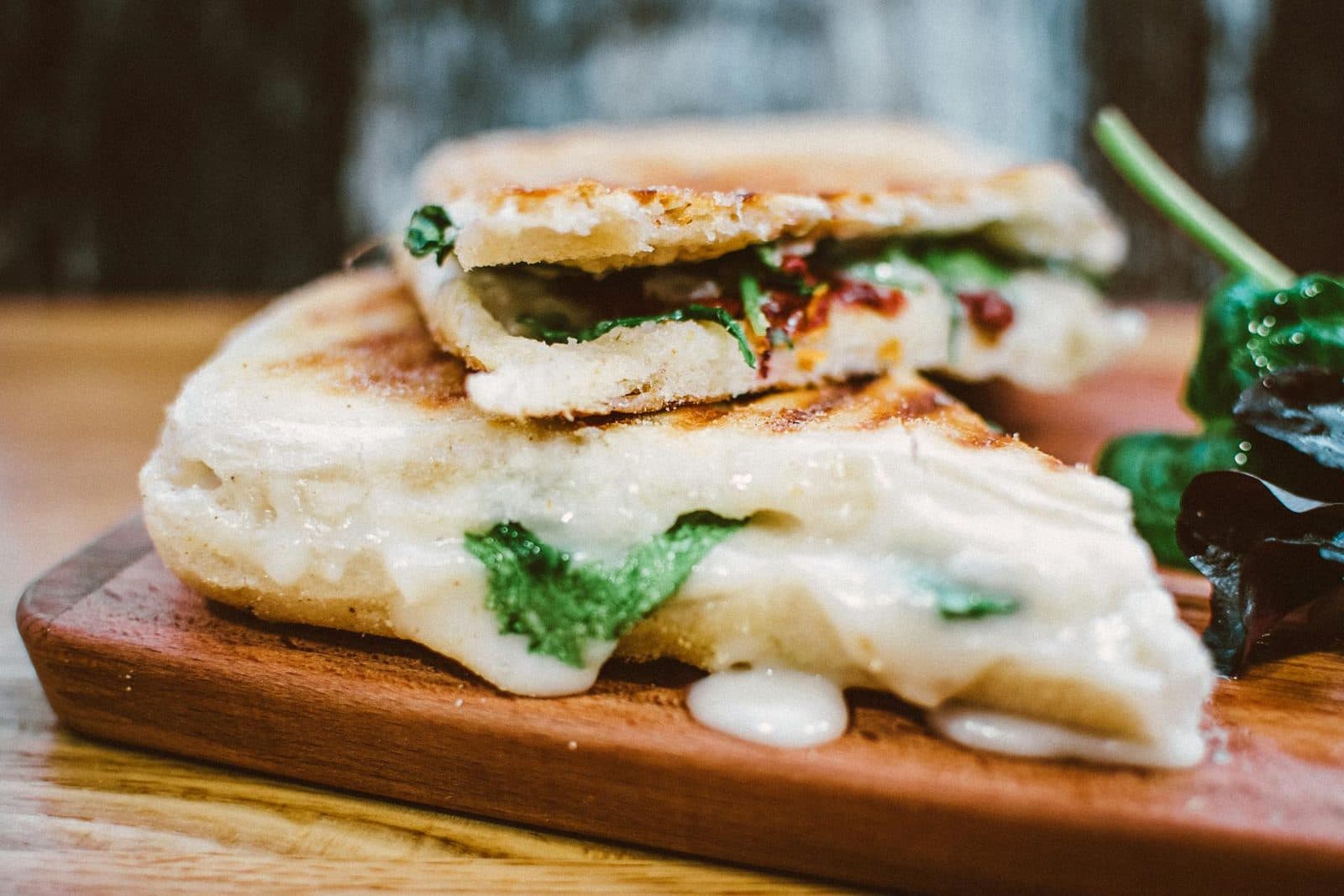 Caprese panini with melted cheese, greens, and toasted bread on a wooden board