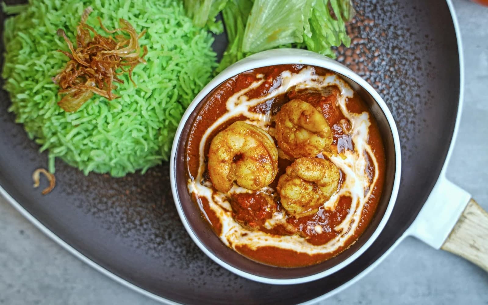 Caribbean coconut curry shrimp in red sauce with green rice on a black plate