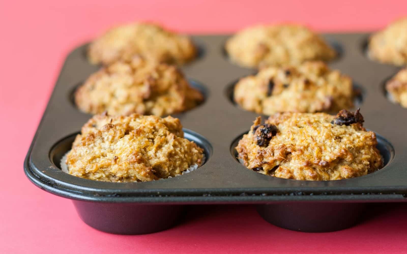 Carrot cake muffins for kids baked in a muffin tin on a pink surface