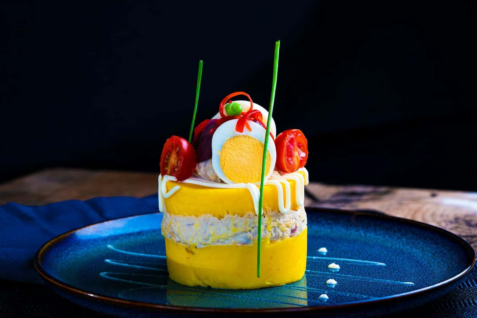 Peruvian causa rellena-style layered potato appetizer with bright garnish on a blue plate