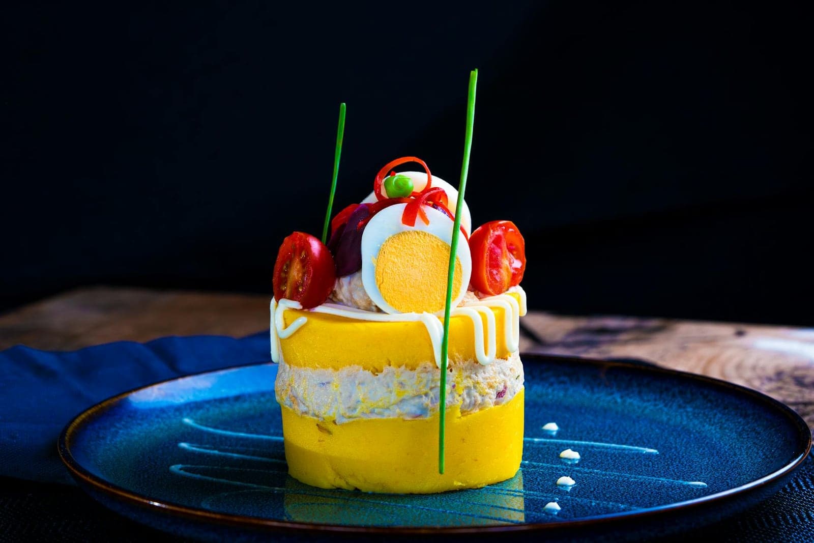 Peruvian causa rellena-style layered potato appetizer with bright garnish on a blue plate