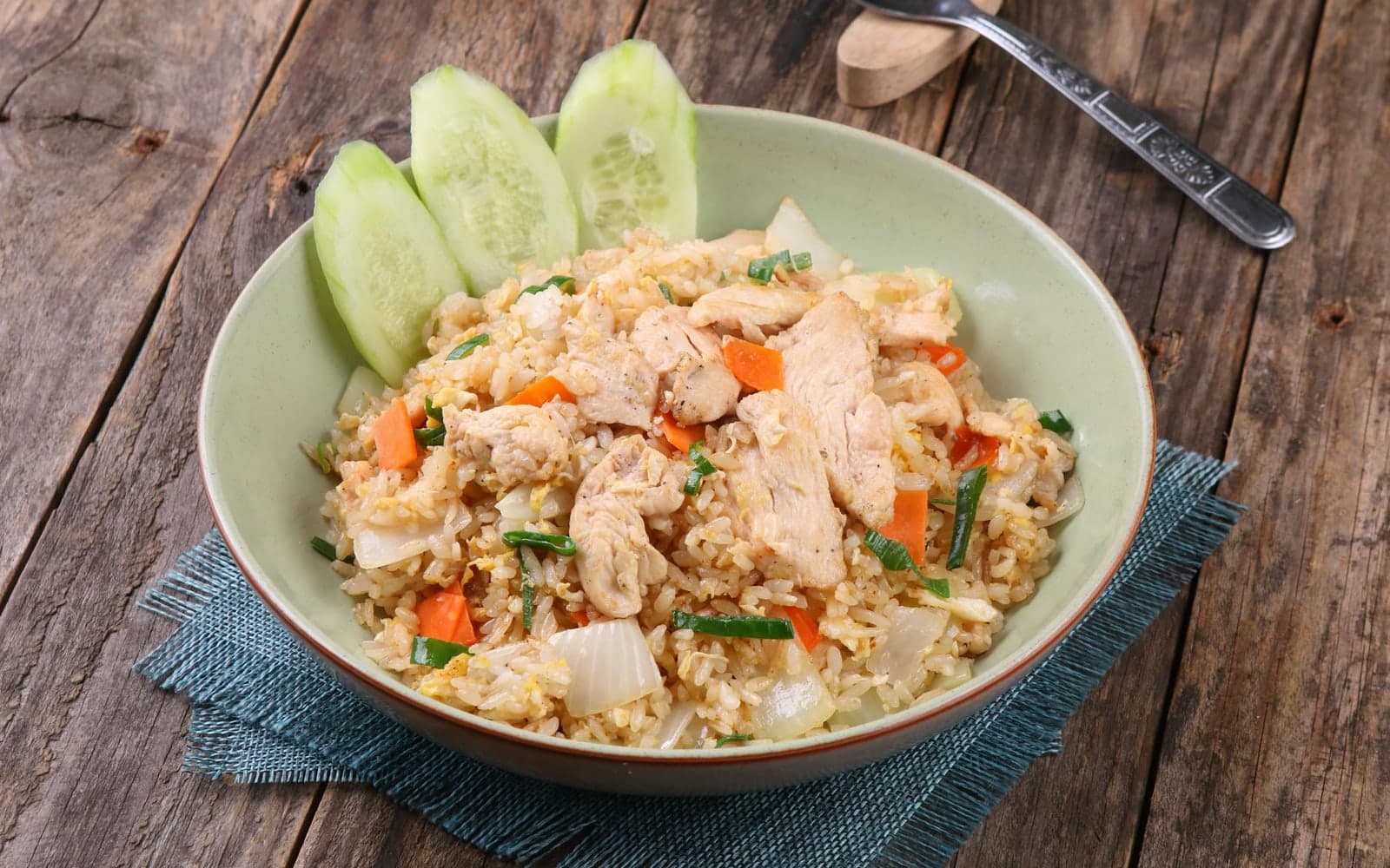 Chicken cauliflower fried rice with vegetables and cucumber slices in a shallow bowl