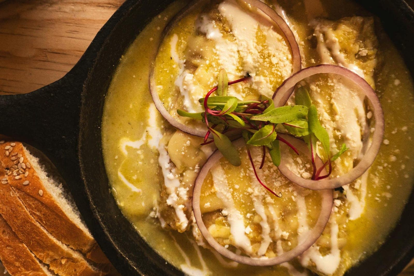 Chicken enchiladas Suizas in green sauce with cheese and red onion in a skillet