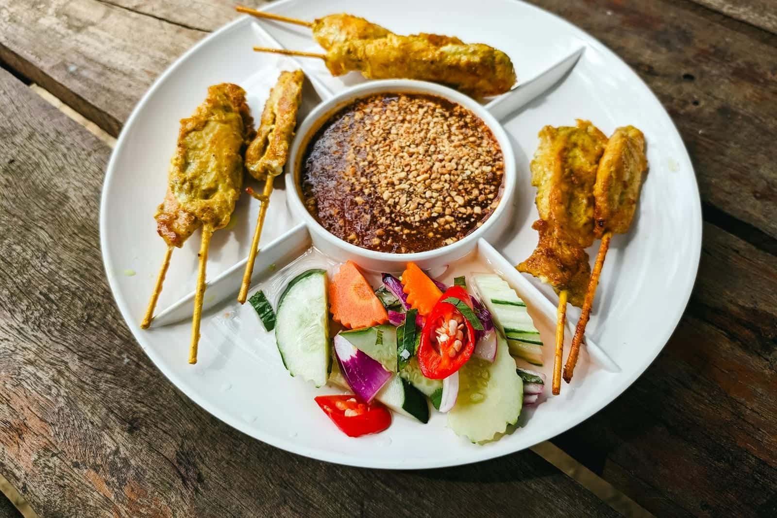 Chicken satay skewers served with peanut sauce, cucumber, chilies, and herbs