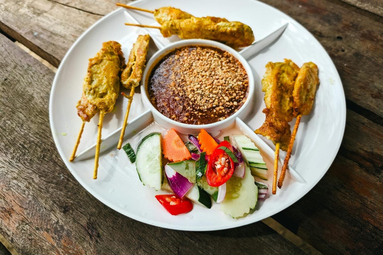 Chicken satay skewers served with peanut sauce, cucumber, chilies, and herbs