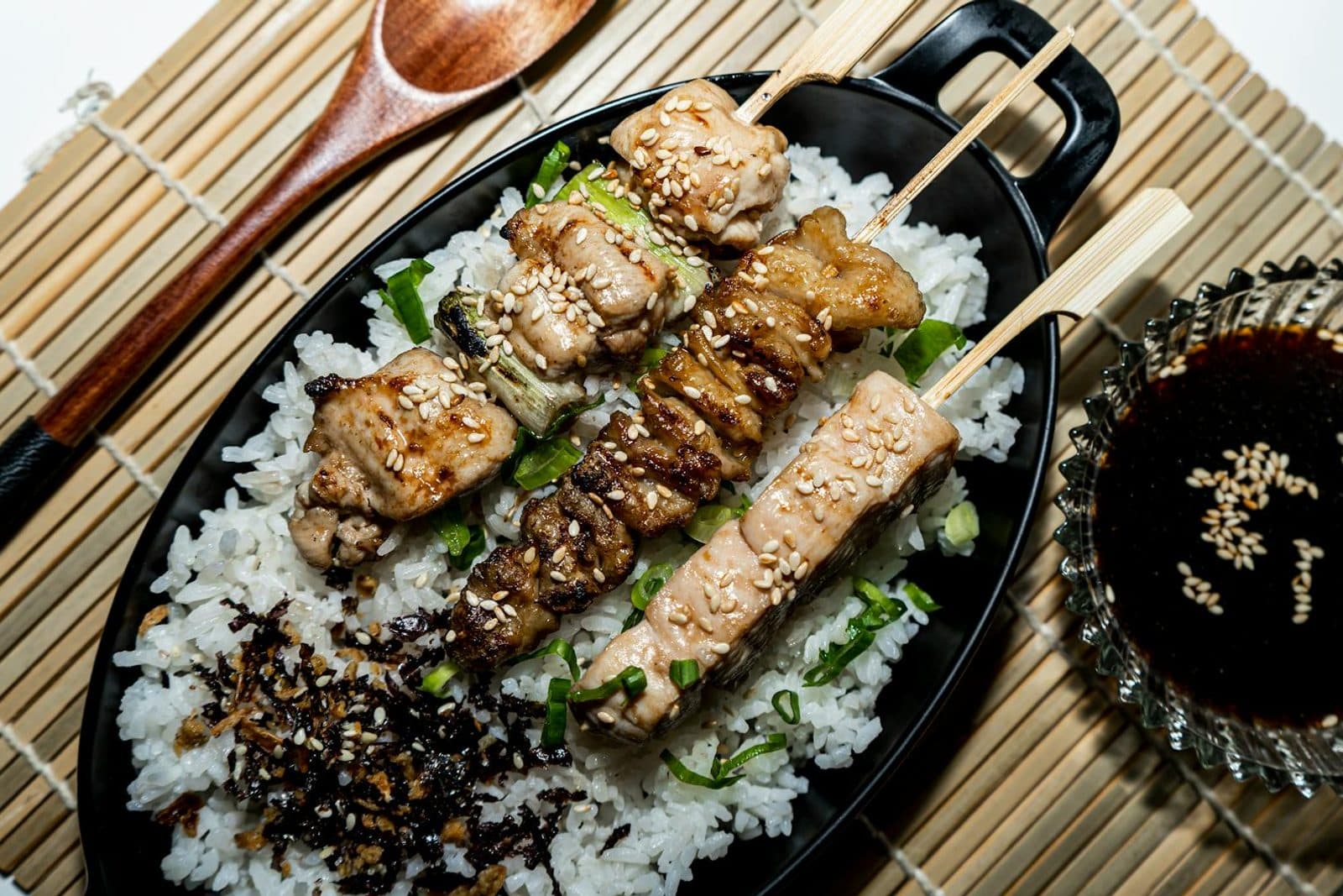 Chicken yakitori skewers served over rice with sesame seeds and dipping sauce