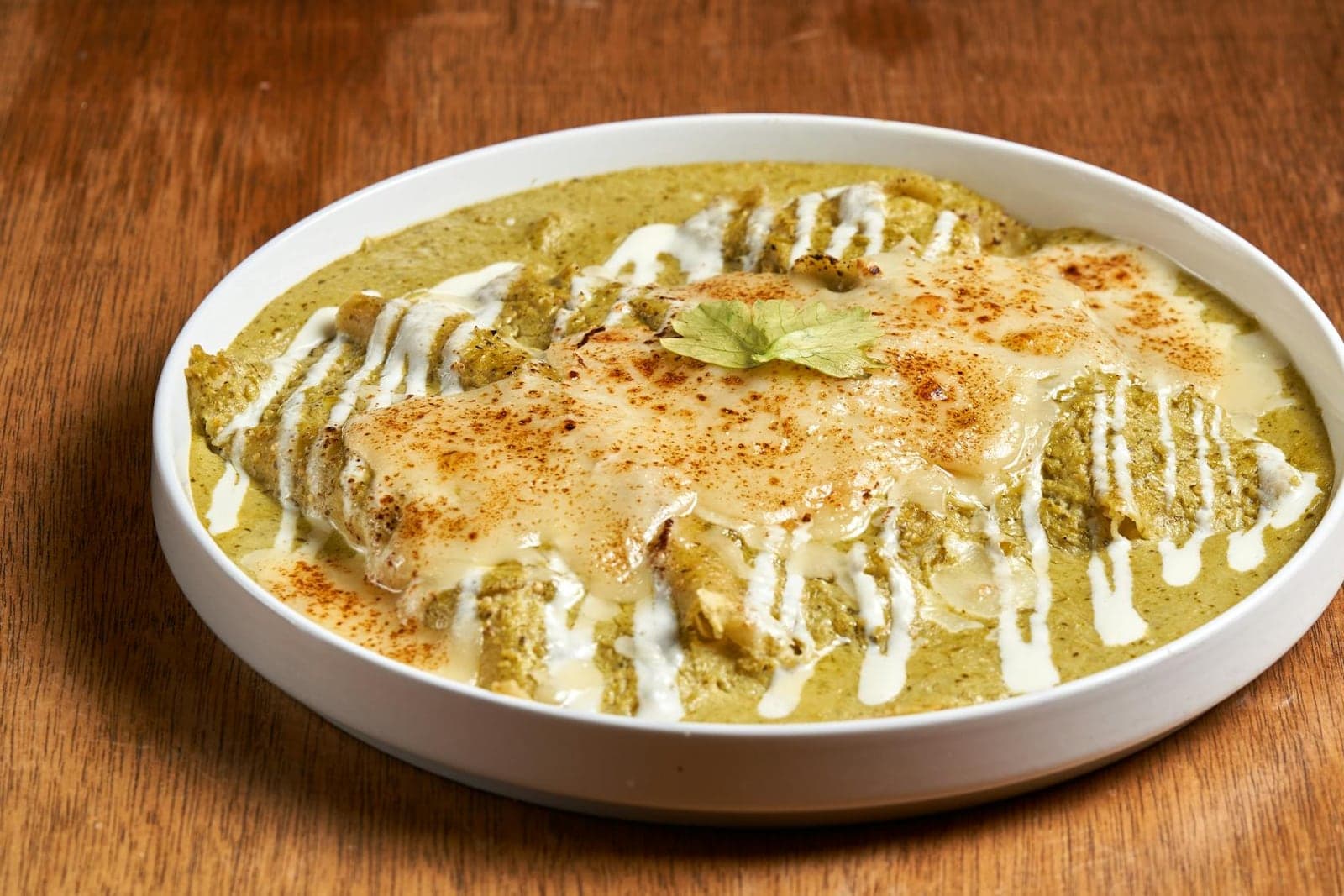 Chilaquiles verdes with tomatillo salsa, crema, cheese, and cilantro in a shallow bowl