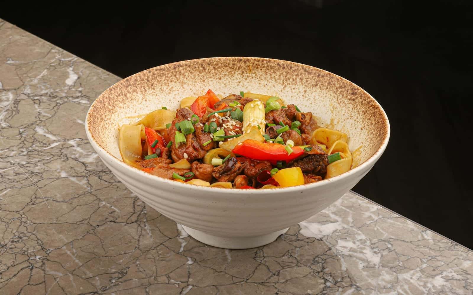 Chinese black pepper beef noodles with peppers and beef in a white bowl