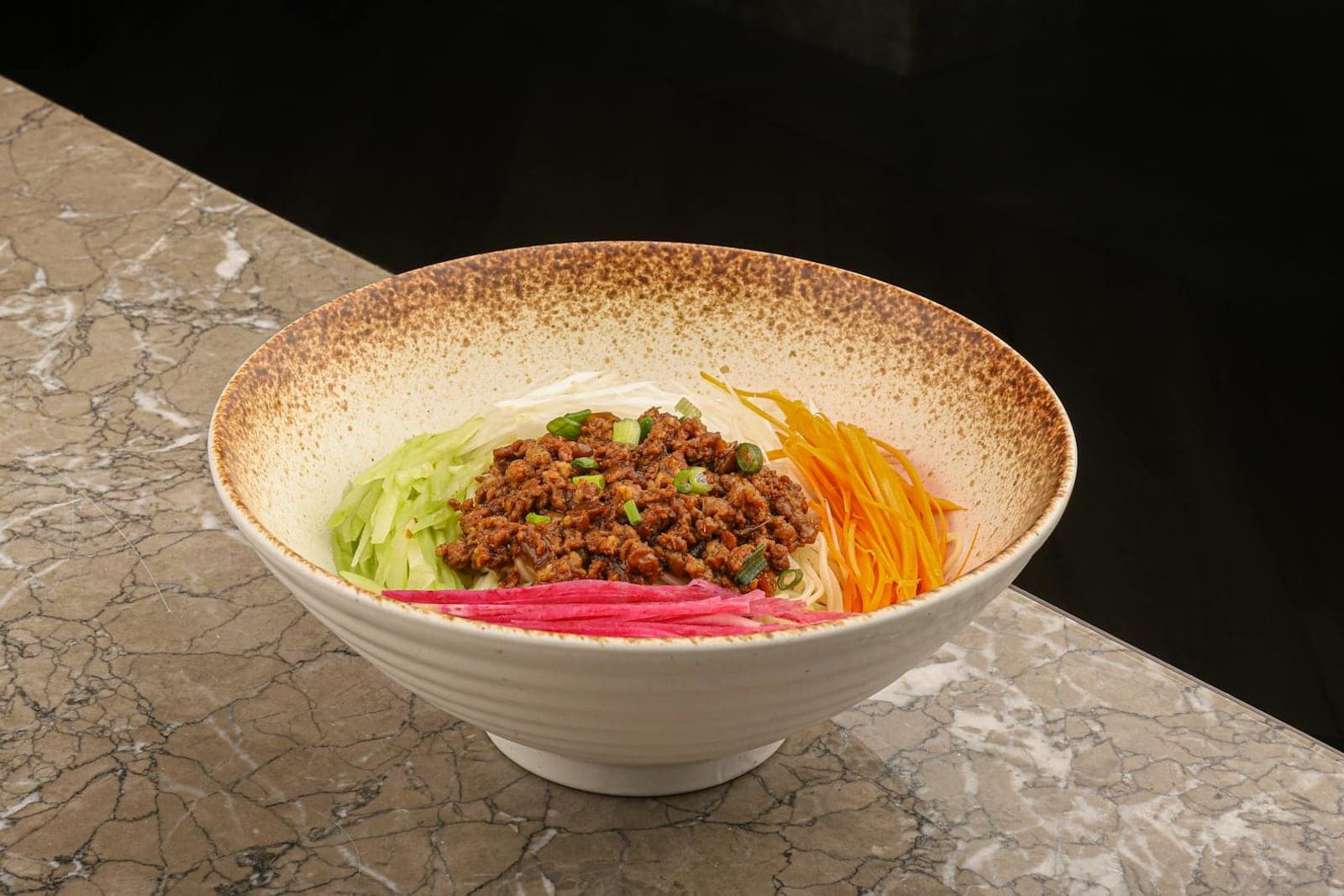 Home-style dan dan noodles with ground meat, vegetables, and chili sauce in a speckled bowl