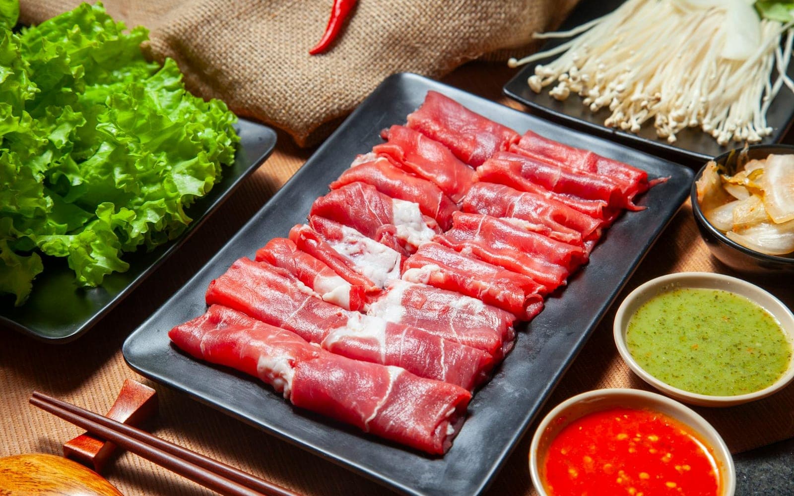 Chinese hot pot ingredients with sliced beef, lettuce, mushrooms, and dipping sauces