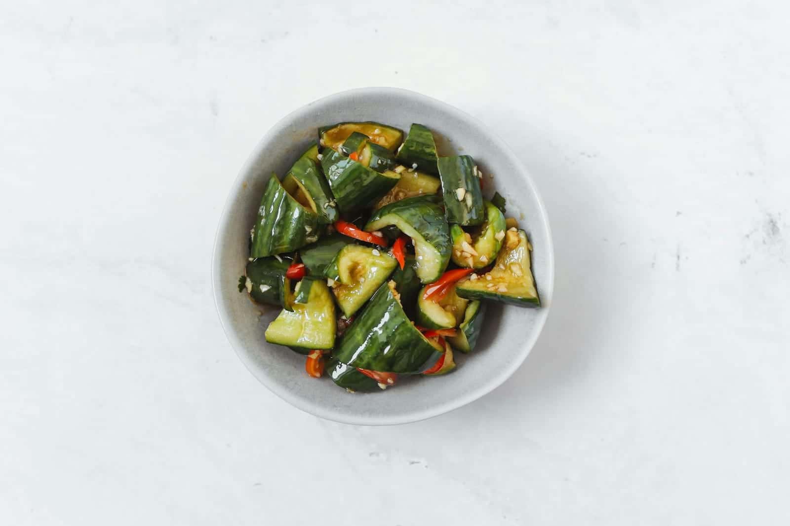 Chinese smashed cucumber salad with cucumber chunks, peppers, and dressing in a white bowl