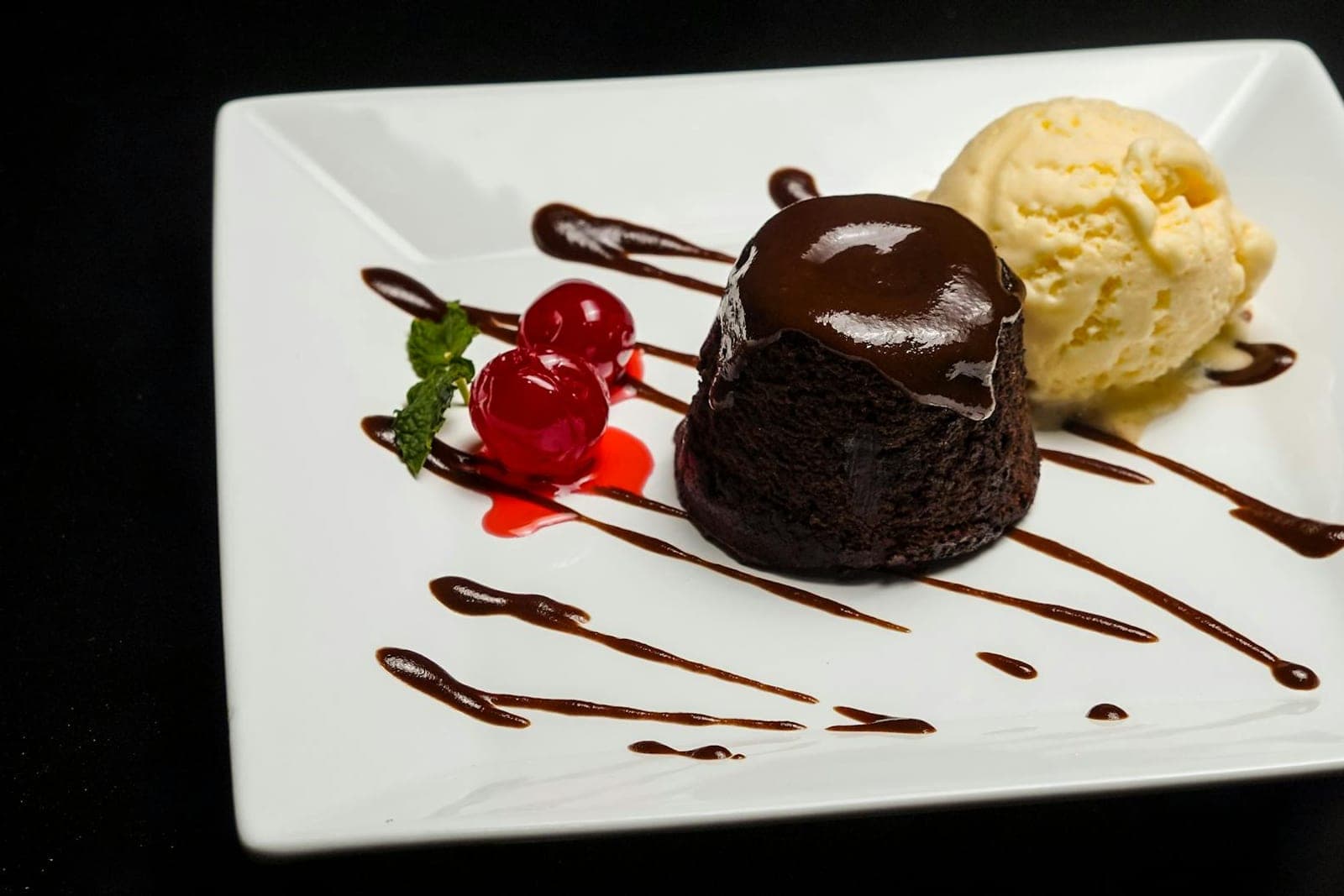 Chocolate lava cake with glossy chocolate sauce, vanilla ice cream, and cherries on a white plate