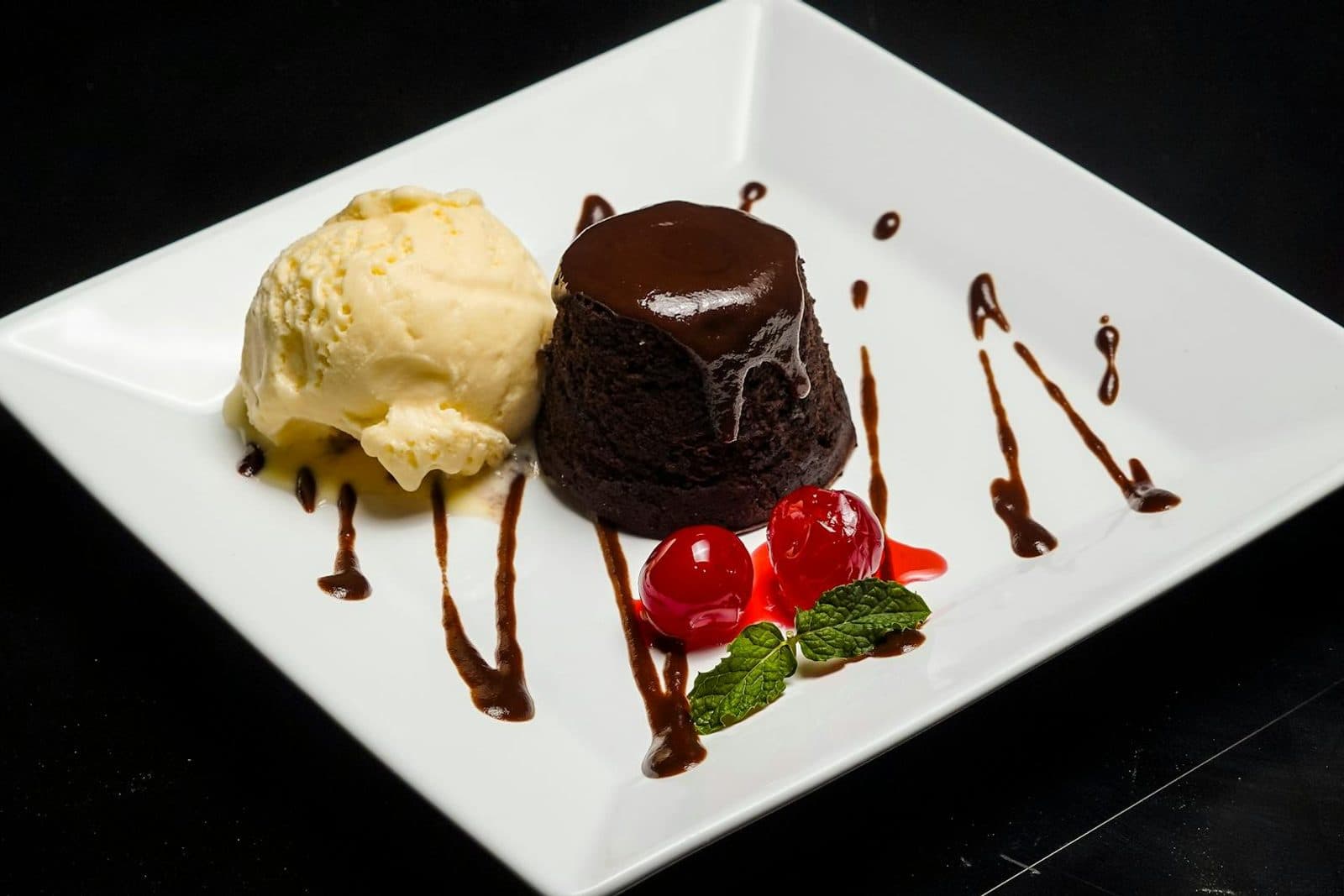 Chocolate lava cakes with molten centers, vanilla ice cream, cherries, and chocolate sauce