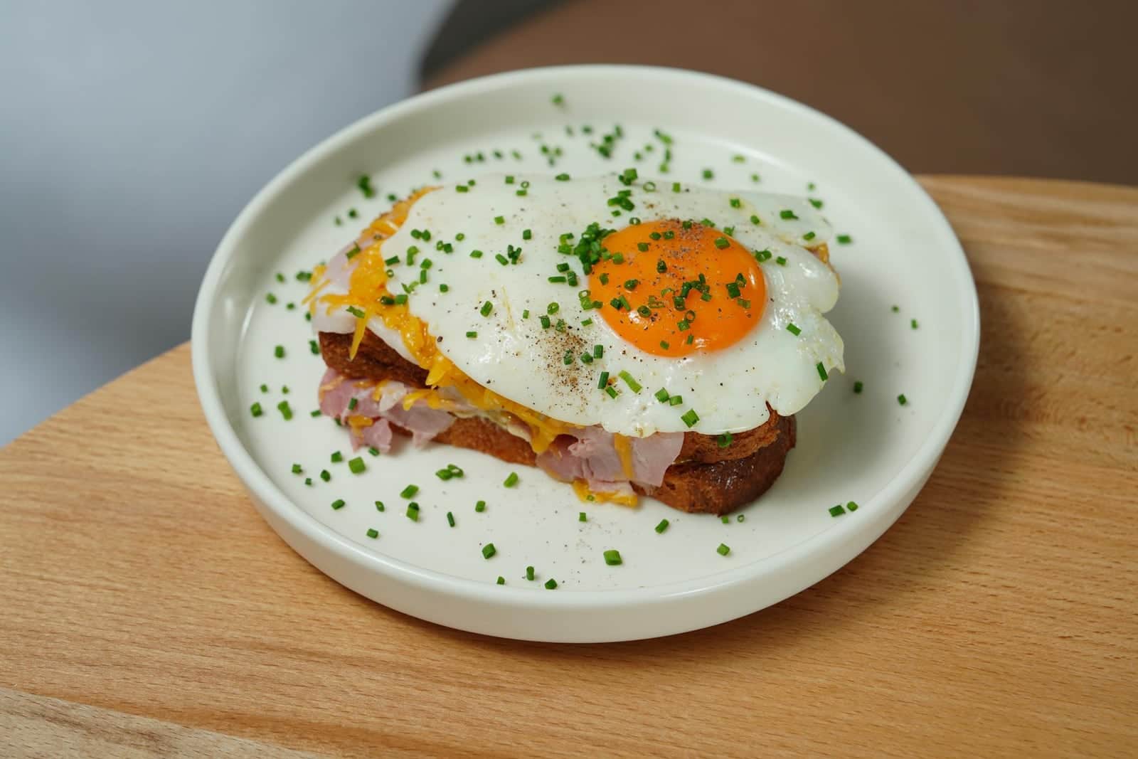 Croque madame sandwich topped with a fried egg and chives on a pale green plate