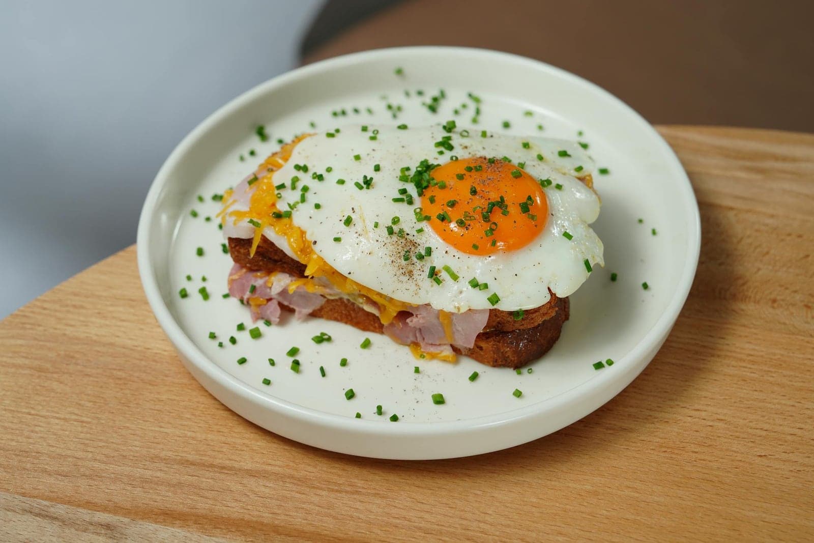 Croque madame sandwich topped with a fried egg and chives on a pale green plate